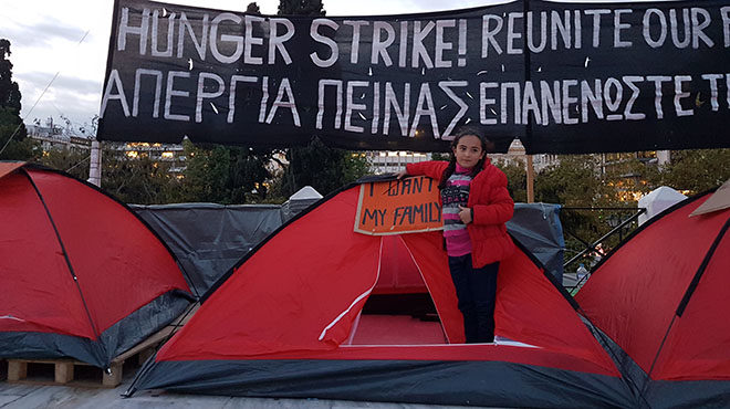 Bild: Mädchen steht vor einem Zelt mit einem Plakat "I want my family", im Hintergrund ein banner auf Englisch und Greichisch, dass den Familiennachzug innerhalb der EU fordert.