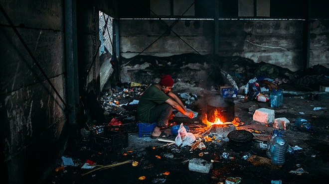 Junger Flüchtling in Bosnien am Feuer in einer Lagerhalle